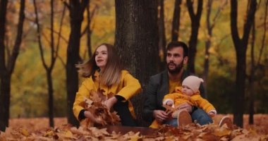 Sonbahar parkında küçük bebeğiyle mutlu bir aile. Annem yapraklarını kusuyor.