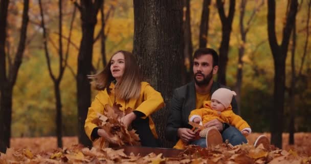 Felice giovane famiglia con bambino piccolo al parco autunnale, la mamma vomita una foglia — Video Stock