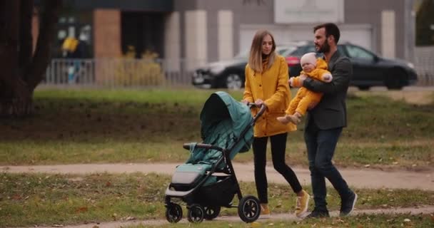 秋の公園で赤ちゃん馬車と一緒に歩く若い家族 — ストック動画