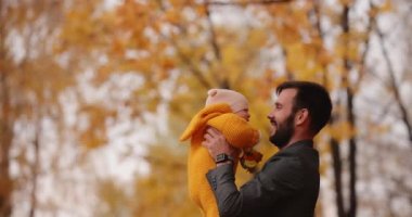 Mutlu baba fırlatır ve bebeğini sonbahar parkında yakalar.