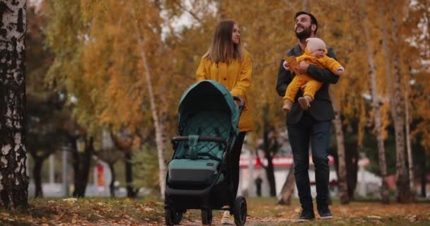 Familia joven caminando con carro de bebé en el parque de otoño — Vídeo de stock