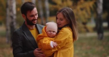 Sonbahar parkında kucağında küçük bir bebek taşıyan mutlu bir aile.