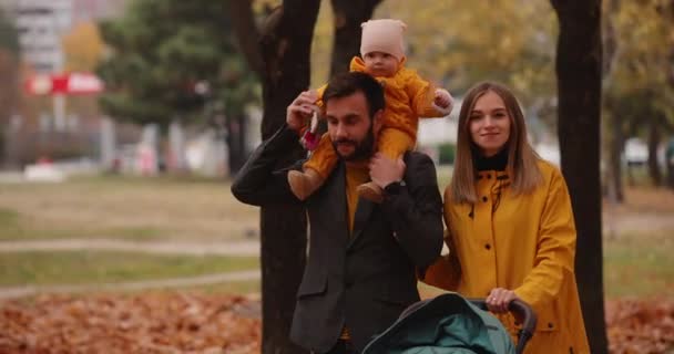 Happy young family walking with baby carriage at the autumn park — Stock Video