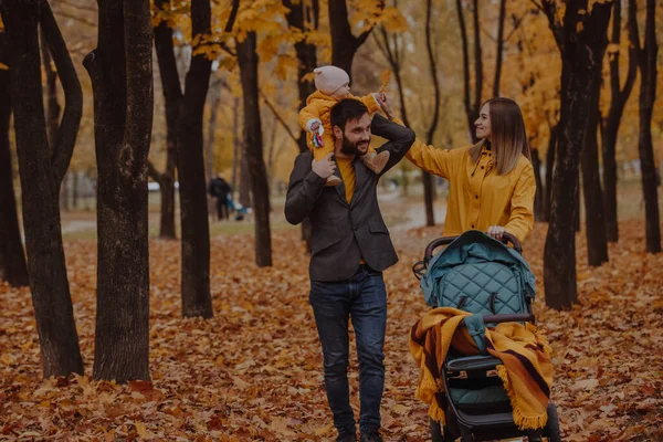 Genç bir aile sonbahar parkında bebek arabasıyla yürüyor. — Stok fotoğraf