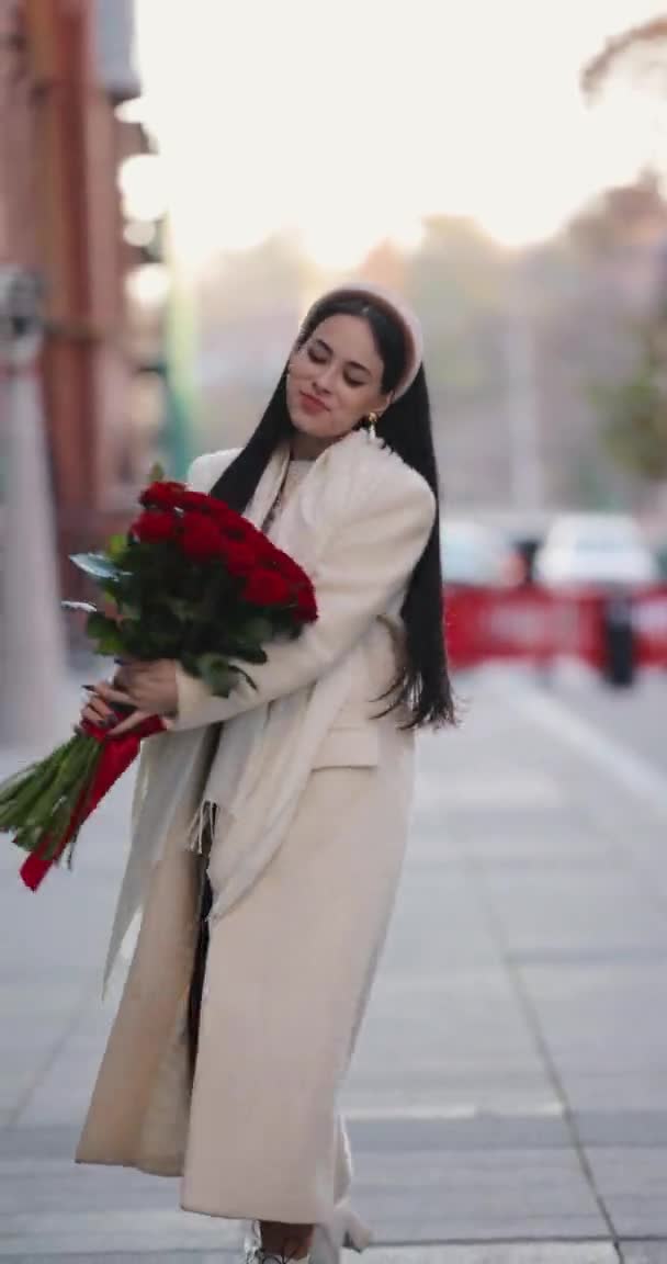 Lycklig kvinna bär och sniffar blommor går runt i staden, vertikal video — Stockvideo