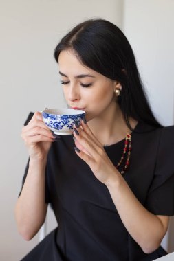 Siyahlı zarif kadın fincandan çay içiyor.
