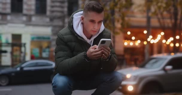 Portrait of cool man using smartphone sitting in the autumn city — Stock Video