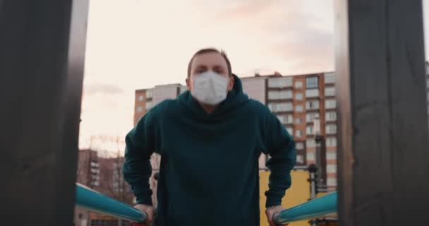 Hombre enojado haciendo flexiones en las barras con máscara quirúrgica — Vídeos de Stock