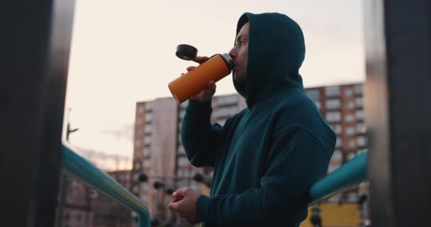 Mann auf dem Sportplatz trinkt Tee aus Thermoskanne — Stockvideo