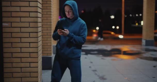 Egy férfi telefonál a falnak támaszkodva egy éjszakai városban. — Stock videók