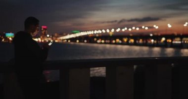 Alacakaranlıkta şehir setinde akıllı telefon kullanan bir adam.