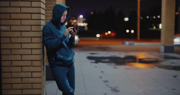 Homem usando telefone inclinado na parede em uma cidade noturna — Vídeo de Stock