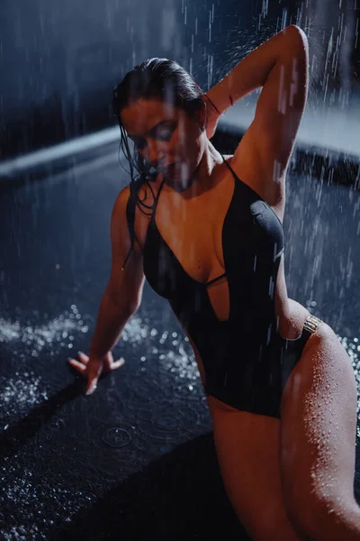 En kvinne i bikini sitter i akvariestudio under regndråper – stockfoto