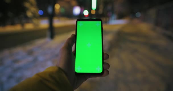 Man met groen scherm in een hand wandelen op besneeuwde stoep — Stockvideo