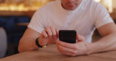 Yakından tanınmayan bir adam bir kafede telefon kullanıyor.