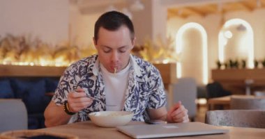 Adam hem kafede makarna yiyip hem de dizüstü bilgisayar kullanıyor.