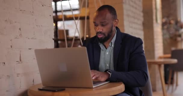 Африканский бизнесмен работает на ноутбуке в кафе — стоковое видео