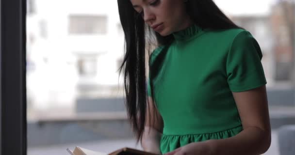 Женщина читает книгу сидя на подоконнике в кафе — стоковое видео