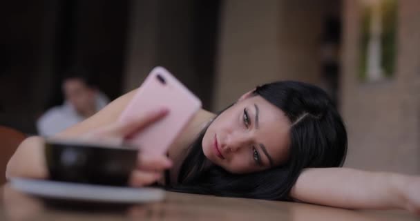 Уставшая женщина с помощью смартфона лежит на столе — стоковое видео