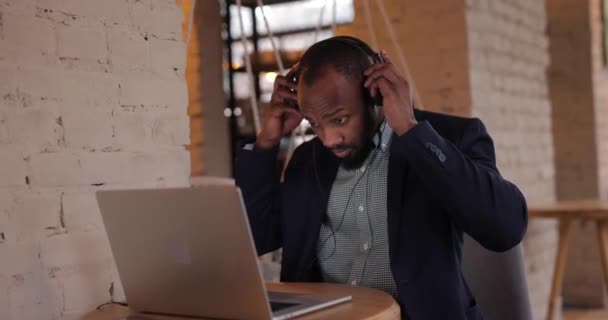 Afrikalı işadamı bilgisayarda kulaklıkla çalışıyor. — Stok video
