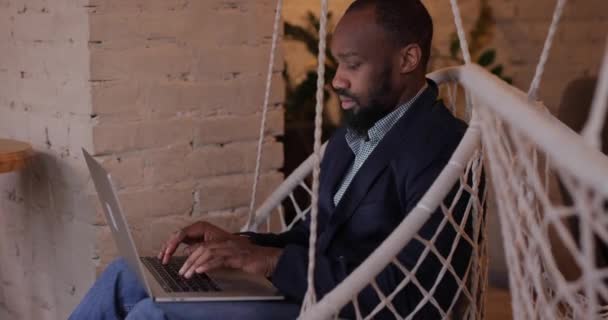 El empresario africano trabaja por el ordenador portátil en la respuesta de la cafetería a la llamada entrante — Vídeos de Stock
