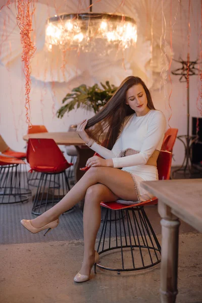 Kaunis nainen tyylikäs valkoinen mekko istuu tuolissa — kuvapankkivalokuva