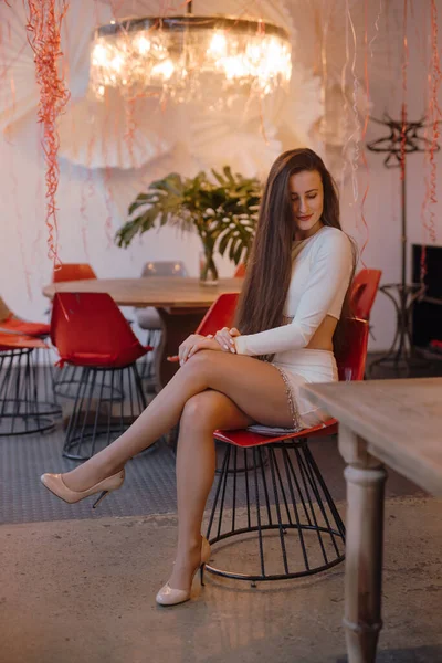 Hübsche Frau im eleganten weißen Kleid auf einem Stuhl sitzend — Stockfoto