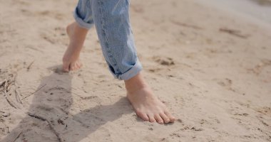 Dişi bacaklar kumda yalınayak yürüyor.