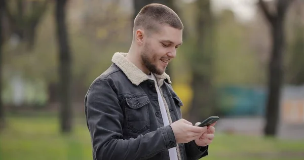 Hombre Sonriente Usar Teléfono Inteligente Caminando Parque Día Primavera —  Fotos de Stock