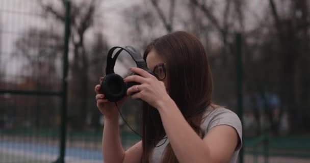 Симпатична дівчина гуляє в парку слухаючи музику в навушниках — стокове відео