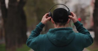 Arkadan bakan adam şehirde yürürken büyük kulaklık takıyor.