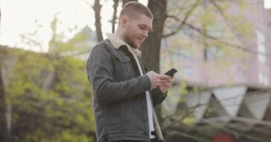 Yavaş çekim gülümseyen adam parkta akıllı telefon kullanıyor.