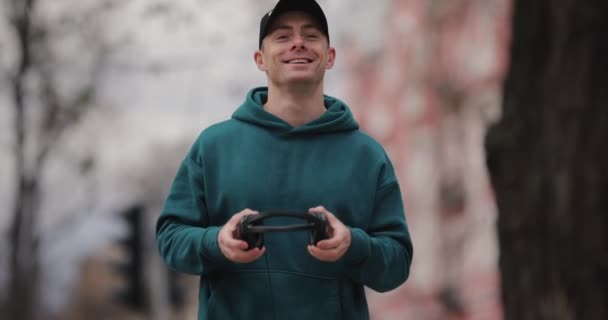 Uśmiechnięty mężczyzna zakłada duże słuchawki spacerując po mieście — Wideo stockowe