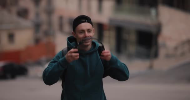 Uśmiechnięty mężczyzna zakłada słuchawki spacerując po mieście — Wideo stockowe