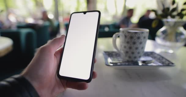 POV tangan laki-laki memegang smartphone dengan layar kosong di kafe — Stok Video