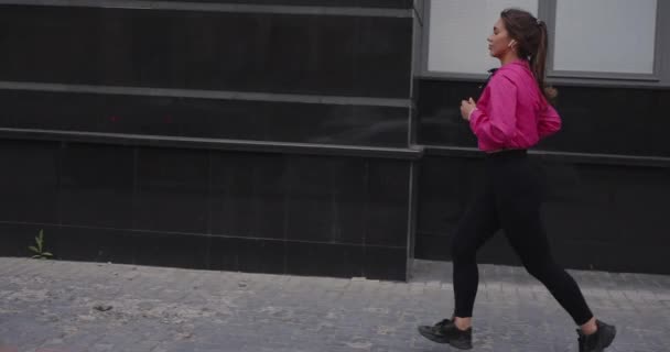 Ziemlich sportliche Frau joggt mit Kopfhörern durch die Stadt und hört Musik — Stockvideo