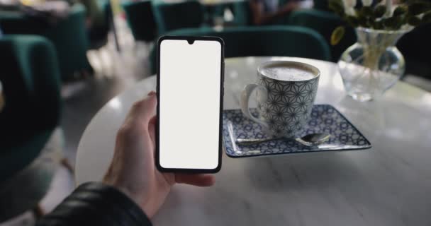 POV mano masculina sosteniendo teléfono inteligente con pantalla en blanco en un café — Vídeos de Stock