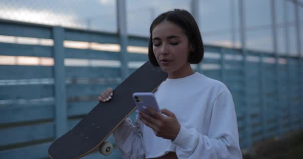 Skateboarding Κορίτσι Περπάτημα Στο Δρόμο Χρησιμοποιώντας Smartphone Και Τσίχλα Αργή — Αρχείο Βίντεο