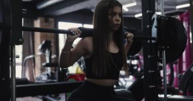 Smith Machine 'in üzerinde halter olan bir kadın spor salonunda çömeliyor.