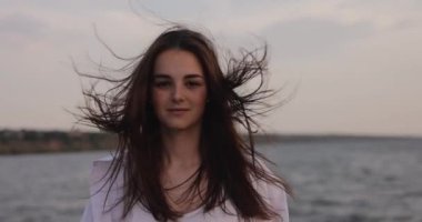 Yavaşça esen rüzgar, iskelede gülümseyen genç bir kadının saçlarını savuruyor.