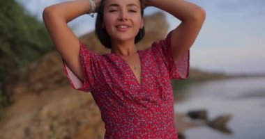 Kumsalda büyük bir taşın yanında yaz elbisesi giymiş güzel bir kadın.