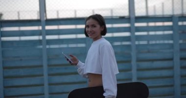 Kaykaycı kız akıllı telefon kullanarak sokakta yürüyor, ağır çekimde.