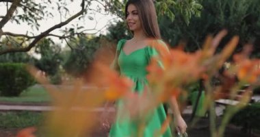 Güzel ve mutlu bir kadın yeşil elbisesiyle parkta yürüyor. Eğleniyor, ağır çekimde.