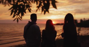 Silhouette of friends looking at sunset standing at the sea beach