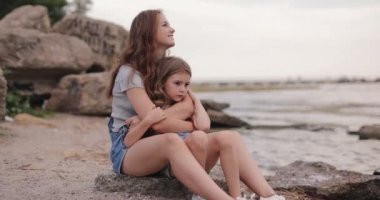 Two cute sisters sitting together at the beach of the sea