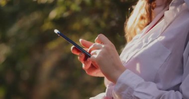 Yaz parkında telefon kullanan genç bir kadın yakın plan bir bankta oturuyor.