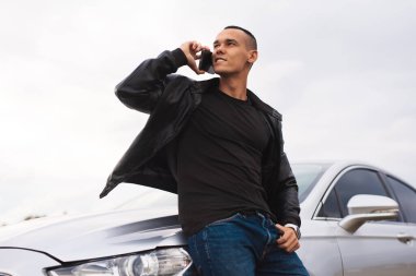 Arabasının yanında telefonla konuşan kendinden emin, başarılı genç bir adam.