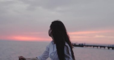 Genç kız deniz manzarasına bakıyor ve bulutlu bir günde kulaklıkla müzik dinliyor.