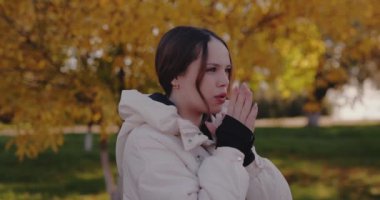 Sonbahar gününde elleri ısıtan genç bir kadın, ağır çekimde.