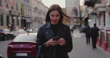 Şehir sokaklarında akıllı telefon kullanan bir kadın ağır çekimde yürüyor.